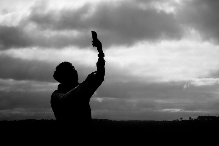 Young man holds up phone outdoors